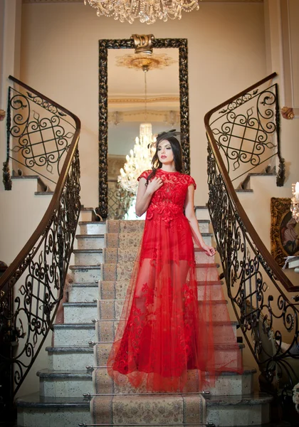 Το όμορφο κορίτσι σε ένα μακρύ κοκκινωπό φόρεμα που θέτουν σε μια εκλεκτής ποιότητας σκηνή. όμορφη κοπέλα φορώντας ένα κόκκινο φόρεμα σε ένα παλαιό ξενοδοχείο. αισθησιακό κομψό νεαρή γυναίκα σε εσωτερική βολή κόκκινο μακρύ φόρεμα. — Φωτογραφία Αρχείου