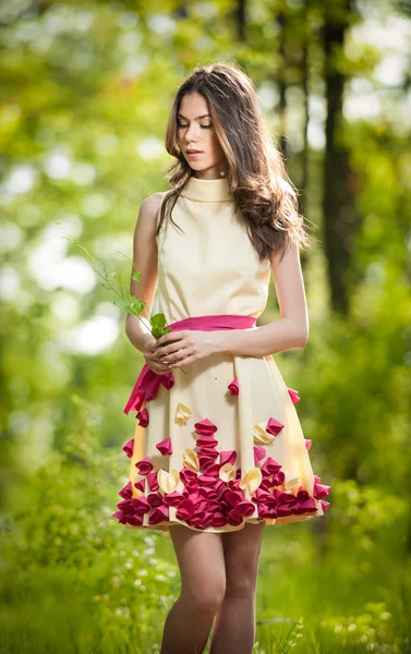 Young beautiful girl in a yellow dress in the woods. Portrait of romantic woman in fairy forest. Stunning fashionable teenage model in summer meadow, outdoor shot. Cute brunette long hair female. — Stock Photo, Image