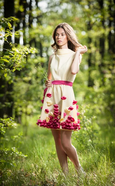 Young beautiful girl in a yellow dress in the woods. Portrait of romantic woman in fairy forest. Stunning fashionable teenage model in summer meadow, outdoor shot. Cute brunette long hair female. — Stock Photo, Image