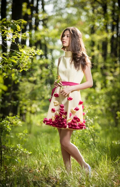 Young beautiful girl in a yellow dress in the woods. Portrait of romantic woman in fairy forest. Stunning fashionable teenage model in summer meadow, outdoor shot. Cute brunette long hair female. — Stock Photo, Image