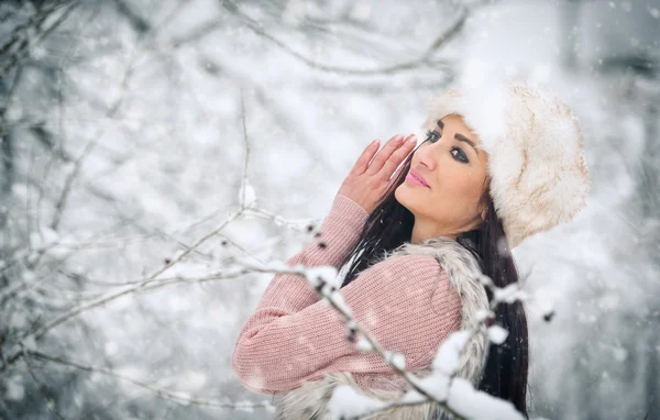 Kvinna med vit pälsmössa leende njuta av vinter landskapet i skogen. Sidovy av glad brunett Tjej leker med snö i vinterlandskap. Vacker ung kvinna på vintern bakgrund — Stockfoto