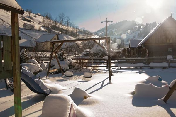Staré dřevěné domy a dřevěné rumunské houpačky sněhem. Chladný zimní den v krajině. Tradiční Karpaty vesnice scenérie, Rumunsko. Venkov loděnice s objekty, které jsou pokryty sněhem — Stock fotografie