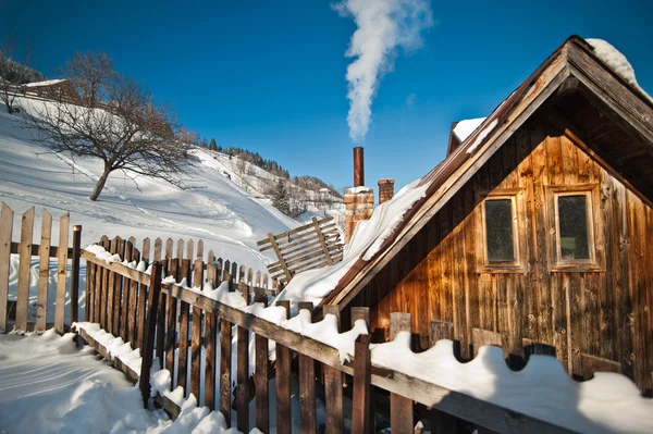 Gamla trähus med hill täcks av snö i bakgrunden. Ljusa kall vinterdag i berg landskap. Karpaterna, Rumänien. Isolerade trä hus stuga fjällstuga täcks av snö — Stockfoto