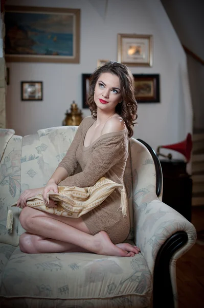 Young sensual woman sitting on sofa relaxing. Beautiful long hair girl with comfortable clothes daydreaming on the couch, alone. Attractive brunette wearing a tight fit short dress in cozy scenery — Stock Photo, Image