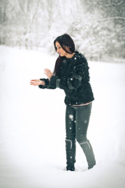 Kar kış manzara ile oynarken mutlu esmer kız görünümünü. Kış arka plan güzel genç kadın. Sıcak yumuşak giysiler içinde bir kış günü açık çekici genç kadın