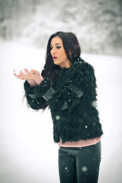 Vista di felice ragazza bruna che gioca con la neve nel paesaggio invernale. Bella giovane femmina su sfondo invernale. Attraente giovane donna in caldi vestiti morbidi all'aperto in una giornata invernale — Foto Stock
