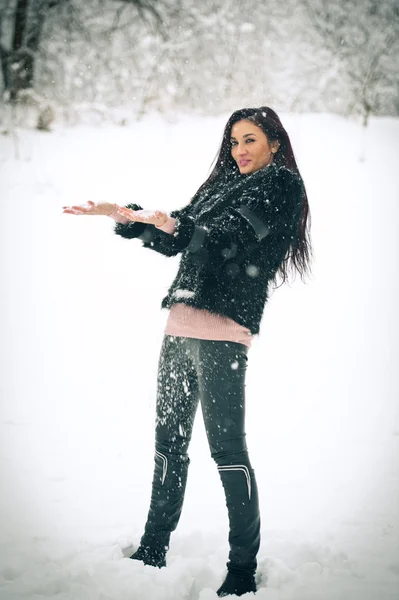 Weergave van gelukkig brunette meisje spelen met sneeuw in de winterlandschap. Mooie jonge vrouw op winter achtergrond. Aantrekkelijke jonge vrouw in warme zachte kleding buiten in een winterdag — Stockfoto