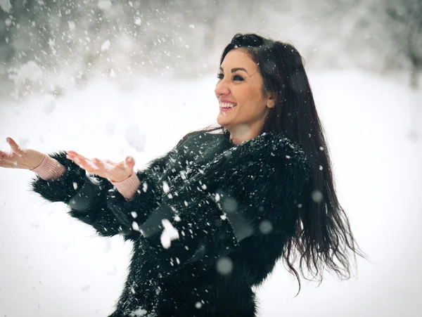 Вид счастливой брюнетки, играющей со снегом в зимнем пейзаже. Молодая самка на зимнем фоне. Привлекательная молодая женщина в теплой мягкой одежде на открытом воздухе в зимний день — стоковое фото