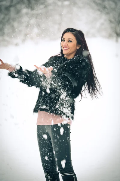 Weergave van gelukkig brunette meisje spelen met sneeuw in de winterlandschap. Mooie jonge vrouw op winter achtergrond. Aantrekkelijke jonge vrouw in warme zachte kleding buiten in een winterdag — Stockfoto