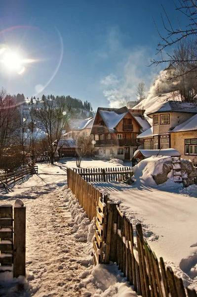 Úzká cesta sněhem na venkov. Zimní krajina s sněžilo stromy, silnice a dřevěného plotu. Chladný zimní den v krajině. Tradiční Karpaty vesnice scenérie, Rumunsko — Stock fotografie