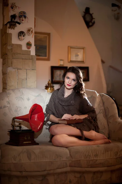 Mooie jonge blote voeten vrouw zittend op de Bank bezit een boek met een rode grammofoon in de buurt van haar boudoir landschap. Aantrekkelijke brunette meisje met lange haren zittend op de Bank, vintage landschap — Stockfoto