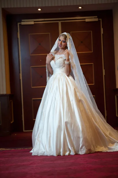 Giovane bella donna di lusso in abito da sposa in posa in interni di lusso. Splendida sposa elegante con lungo velo. Ritratto a figura intera di seducente sposa bionda con abito alla moda, tiro al coperto — Foto Stock