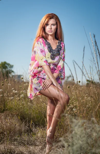 Belle jeune femme dans le champ de fleurs sauvages sur fond de ciel bleu. Portrait de jolie fille rousse aux cheveux longs relaxant dans la nature, prise de vue en plein air. Dame en robe multicolore profitant de la nature — Photo