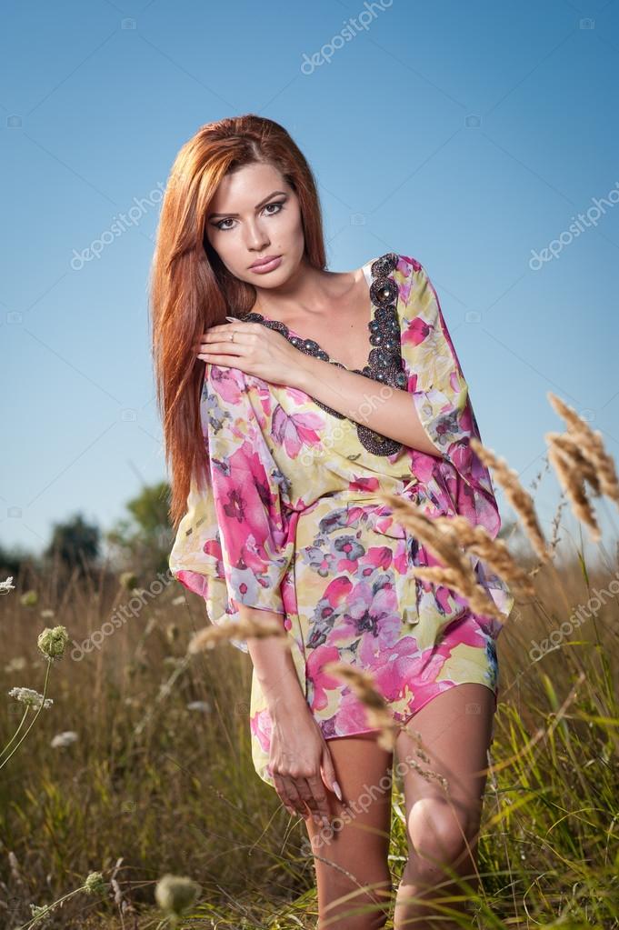 Beautiful young woman in wild flowers field on blue sky background ...