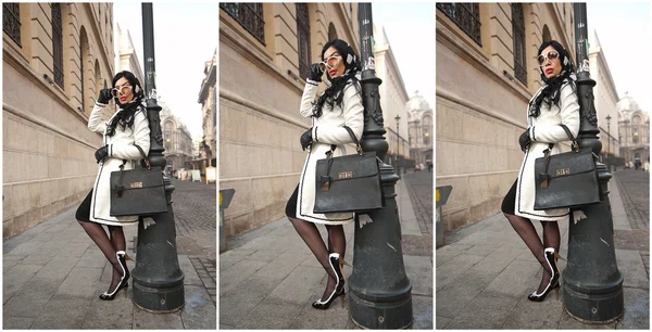 Atractiva joven en una foto de moda de invierno. Hermosa chica joven de moda en blanco y negro posando contra un pilar. Elegante morena con pañuelo en la cabeza, gafas de sol y bolso en el paisaje urbano . — Foto de Stock