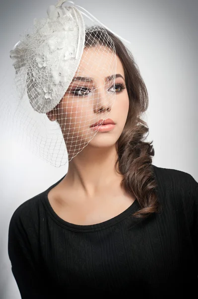 Hairstyle and make up - beautiful young girl art portrait. Cute brunette with white cap and veil, studio shot. Attractive female with beautiful lips and eyes in black blouse, over white — Stock Photo, Image