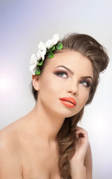Portrait of beautiful girl in studio with white flowers arrangement in her hair and naked shoulders. Sexy young woman with professional makeup and flowers. Creative hairstyle and makeup, studio shot — Stock Photo, Image