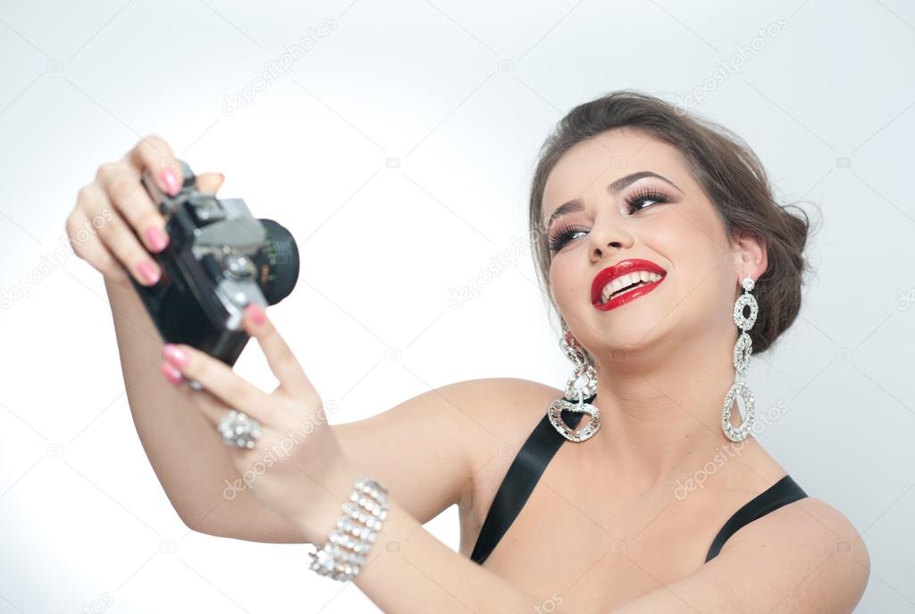 Beautiful young girl with creative make-up and hair style taking photos of herself with a camera. Fashionable attractive woman taking a self portrait. Selfie, indoor, horizontal, over white.