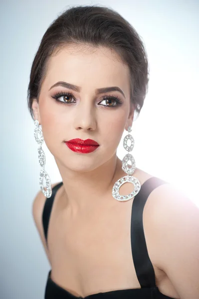 El peinado y el maquillaje - el retrato hermoso femenino artístico con los pendientes. Elegancia. Genuina morena natural con joyas en estudio. Retrato de una mujer atractiva con labios rojos y maquillaje creativo —  Fotos de Stock