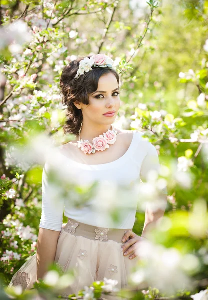 Retrato de una hermosa niña posando al aire libre con flores de los cerezos en flor durante un brillante día de primavera. Atractiva mujer morena con flores accesorios en huerto, tiro de primavera — Foto de Stock