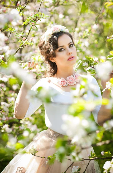 Retrato de una hermosa niña posando al aire libre con flores de los cerezos en flor durante un brillante día de primavera. Atractiva mujer morena con flores accesorios en huerto, tiro de primavera —  Fotos de Stock