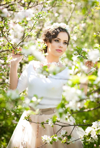 Portrait of beautiful girl posing outdoor with flowers of the cherry trees in blossom during a bright spring day. Attractive brunette woman with flowers accessories in orchard, spring shot — Stock Photo, Image