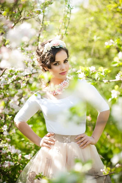 Portrait of beautiful girl posing outdoor with flowers of the cherry trees in blossom during a bright spring day. Attractive brunette woman with flowers accessories in orchard, spring shot — Stock Photo, Image