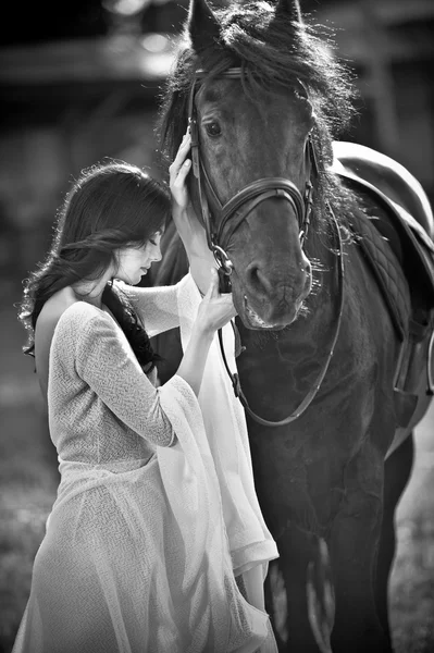 Dame à la mode avec robe de mariée blanche près du cheval brun. Belle jeune femme dans une longue robe posant avec un cheval noir amical. Attrayant élégant femelle avec cheval, gros plan photo — Photo