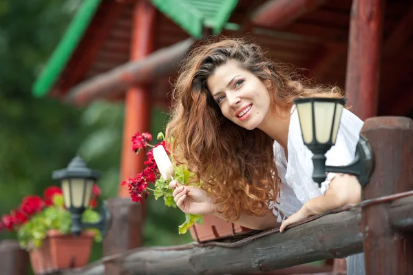 Hermoso retrato femenino con cabello castaño largo comiendo helado cerca de una olla con flores rojas al aire libre. Atractiva mujer con hermosos ojos sonriendo disfrutando de un helado en un día de verano, al aire libre —  Fotos de Stock