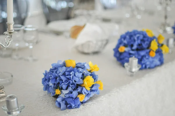 Belos buquês de flores azuis e amarelas, na mesa de casamento. Arranjo de casamento com dois buquês de noiva. Bouquets de casamento elegantes na mesa no restaurante — Fotografia de Stock