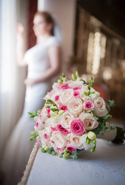 Mariée dans cadre de fenêtre et bouquet de mariage au premier plan. Bouquet de mariage avec une femme en robe de mariée en arrière-plan. Beau bouquet de fleurs roses et blanches. Bouquet de mariage élégant — Photo