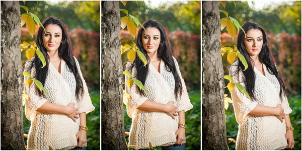 Mulher bonita em branco posando no parque outonal. Jovem morena passando tempo no outono perto de uma árvore na floresta. Longo cabelo escuro mulher atraente sorrindo com folhas desbotadas ao redor dela, ao ar livre — Fotografia de Stock