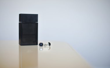 Black perfume bottle and silver cuff-links isolated on gray background. Wedding accessories.