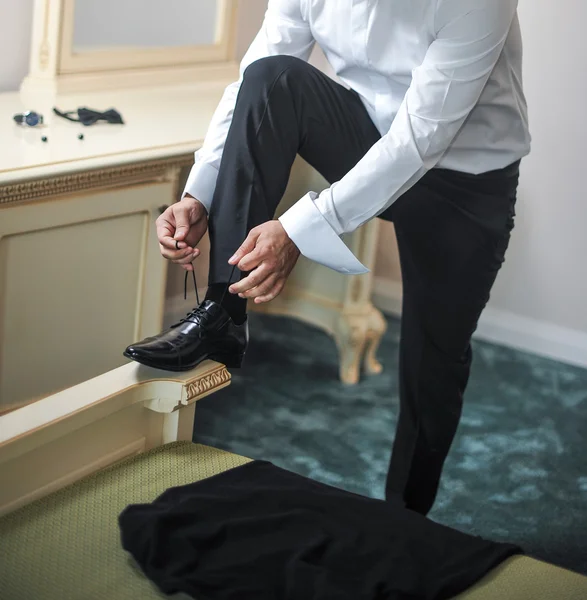 Paras mies valmistautuu erityistä päivää varten. Sulhanen laittaa kengät jalkaan pukeutuessaan juhlapukuun. Sulhasen puku — kuvapankkivalokuva