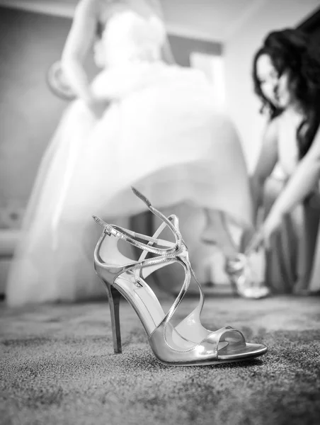 Boda de plata zapato primer plano con una novia en el fondo. Zapato de novia de tacón alto en alfombra. Novia preparándose para un día especial. Mujer en vestido de novia poniéndose zapatos mientras se viste con ropa formal —  Fotos de Stock