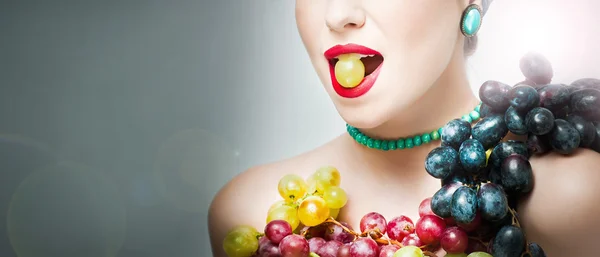 Hermoso maquillaje creativo en el concepto de otoño, plano de estudio sobre fondo gris. Chica modelo de belleza con arreglo de uvas. Hermosa mujer sosteniendo una uva en la boca. Disposición de uvas multicolores —  Fotos de Stock