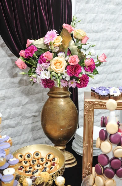 Decoración de la boda con rosas multicolores en jarrón, pastelitos de colores pastel, merengues, magdalenas y macarrones. Elegante y lujoso arreglo de eventos. Postre de boda con macarrones y flores —  Fotos de Stock