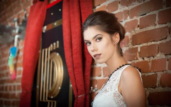 Charming young brunette woman in white lace blouse near a red brick wall. Attractive gorgeous young woman daydreaming near old wall, indoors. Beautiful portrait of a young girl with creative haircut — Stock Photo, Image