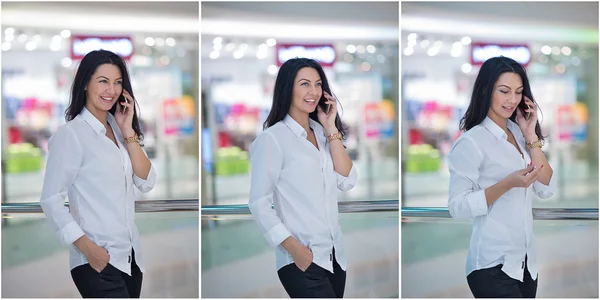 Attractive woman speaking on mobile in mall. Beautiful fashionable young girl in white male shirt posing in modern shopping center. Casual long hair brunette posing smiling talking on mobile indoor. — Stock Photo, Image