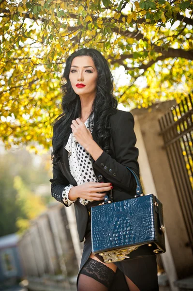 Mujer joven atractiva en una foto de moda otoñal. Hermosa dama de moda en traje blanco y negro posando provocativamente en el parque. Elegante morena en el paisaje de otoño y árboles descoloridos en el fondo  . — Foto de Stock