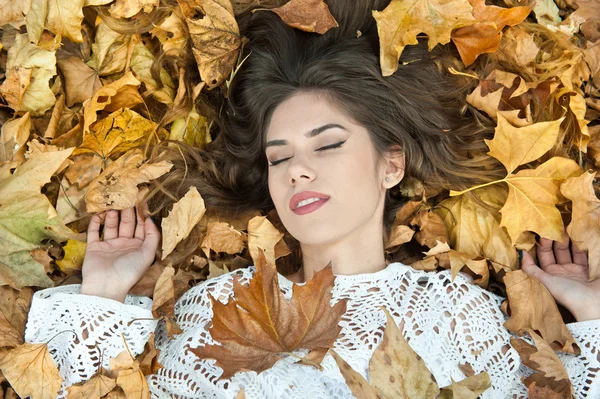 Hodná holka pokrytá podzimními listy. Mladá žena ležící na zemi pokrytá podzimním listím v parku. Krásná sexy dívka ležící na podzimním listí. Mladá žena pokrytá zlatými podzimními listy — Stock fotografie