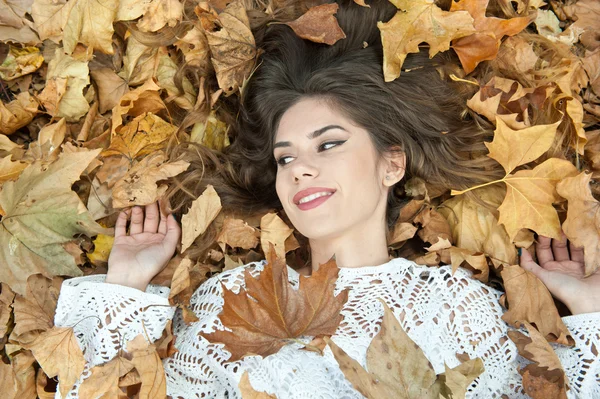 Miła dziewczyna pokryta jesiennymi liśćmi. Młoda kobieta leżąca na ziemi pokryta jesiennymi liśćmi w parku. Piękna seksowna dziewczyna leżąca na jesiennych liściach. Młoda kobieta pokryta złotymi jesiennymi liśćmi — Zdjęcie stockowe
