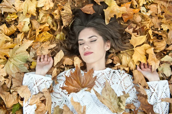 Aardig meisje bedekt met herfstbladeren. Jonge vrouw ligt op de grond bedekt met herfstgebladerte in het park. Mooi sexy meisje liggend op herfstbladeren. Jonge vrouw bedekt met gouden herfstbladeren — Stockfoto