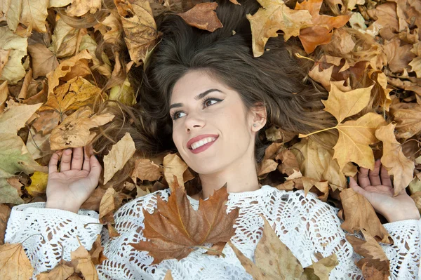 Hodná holka pokrytá podzimními listy. Mladá žena ležící na zemi pokrytá podzimním listím v parku. Krásná sexy dívka ležící na podzimním listí. Mladá žena pokrytá zlatými podzimními listy — Stock fotografie