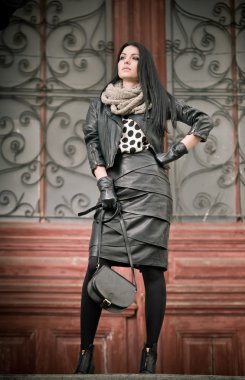 çekici genç kadın kış moda süslenmiş Ferforje kapı arka planda ile vurdu. güzel moda erkek - siyah deri bir kıyafet. şık uzun saçlı esmer kentsel sahne poz.