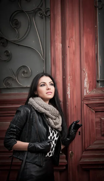 Jovem mulher atraente no inverno moda tiro com ferro forjado portas decoradas no fundo. Bela mulher na moda - roupa de couro preta. Morena de cabelo longo elegante posando em cenário urbano . — Fotografia de Stock