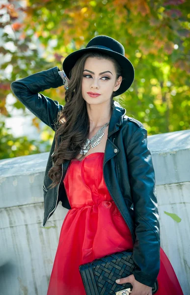 美丽的女人，与在秋季公园构成的黑帽子。花时间在秋天期间在森林的年轻黑妞。长头发迷人创意化妆和红色连衣裙的女孩，在户外拍摄在秋天 — 图库照片