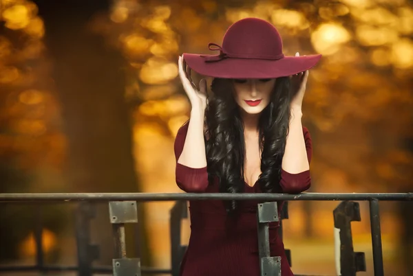 Attraente giovane donna con cappello grande di colore bordeaux in modo autunnale girato. Bella signora misteriosa che copre il viso con il cappello. Elegante bruna con splendida bocca, all'aperto girato in autunno . — Foto Stock