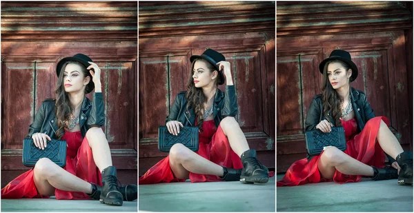 Joven mujer morena hermosa con vestido corto rojo y sombrero negro posando sensual en el paisaje vintage. Romántico misteriosa joven relajante sentado en el suelo contra la pared de madera vintage —  Fotos de Stock