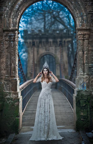 Schöne junge Dame in elegantem weißen Kleid und silbernem Diadem posiert auf einer alten Brücke, Eisprinzessinnen-Konzept. hübsches brünettes Mädchen im langen Hochzeitskleid posiert in winterlicher Landschaft, gotische Eiskönigin — Stockfoto